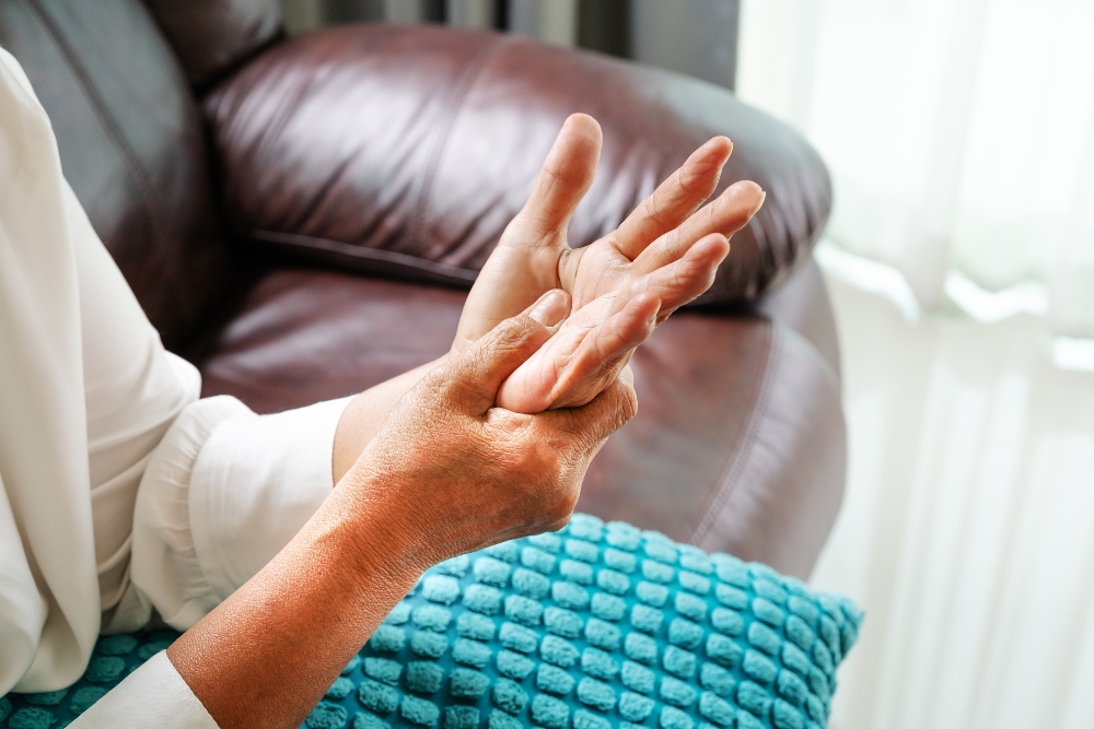 Person holding one open hand in the other beside a leather couch, a visual for joint protection techniques